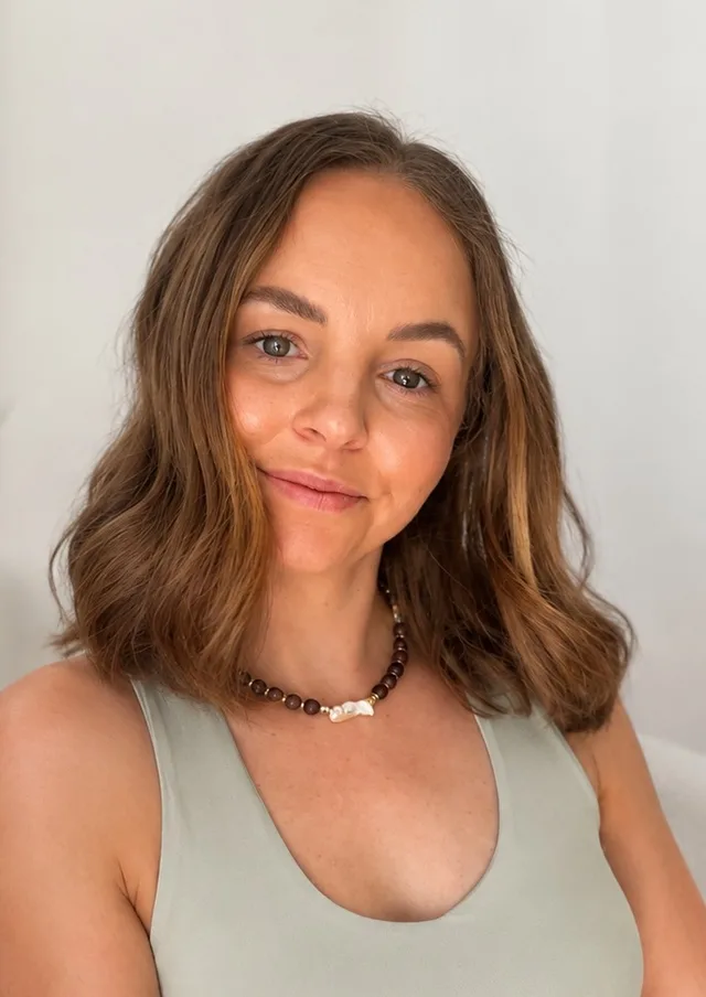 Paige Sawkins, smiling, in a sage green top and a beaded necklace.